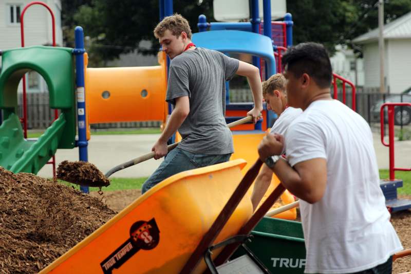 a group of men pushing a wheelbarrow with dirt
