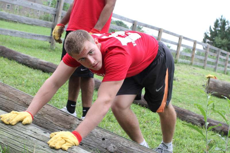a man in a red shirt and black shorts bending over on a wooden plank