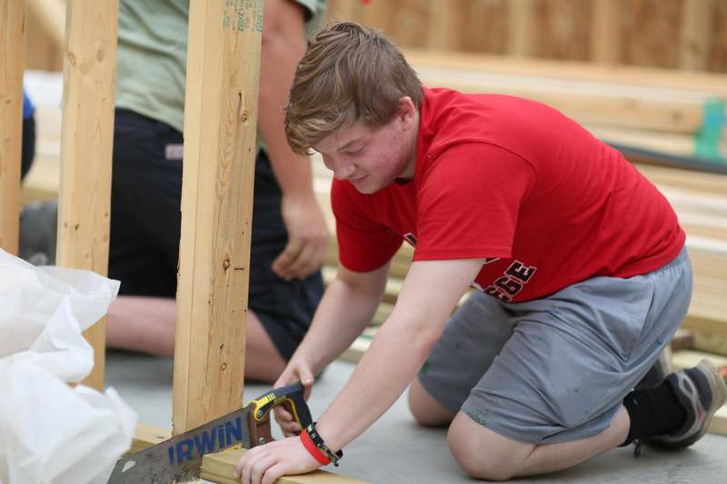 a man in a red shirt cutting a wood beam