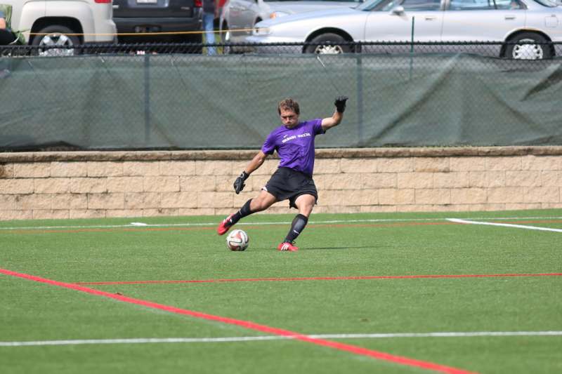 a man in a purple shirt kicking a football ball
