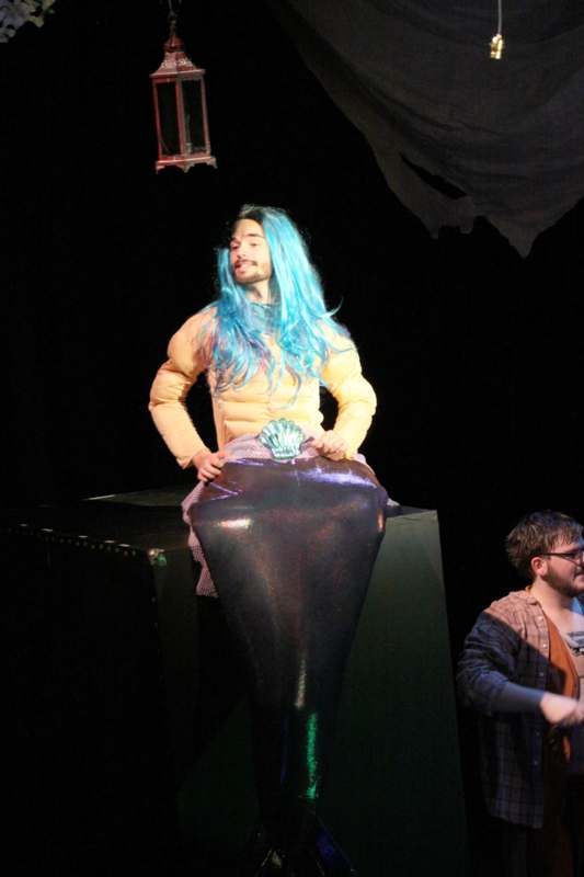 a man with blue hair and a mermaid tail on a stage