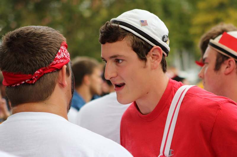 a man in a red shirt and white hat talking to another man