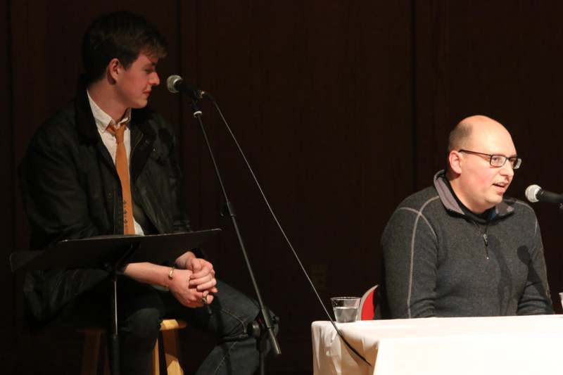 a man sitting at a table with a microphone and a man sitting at a table