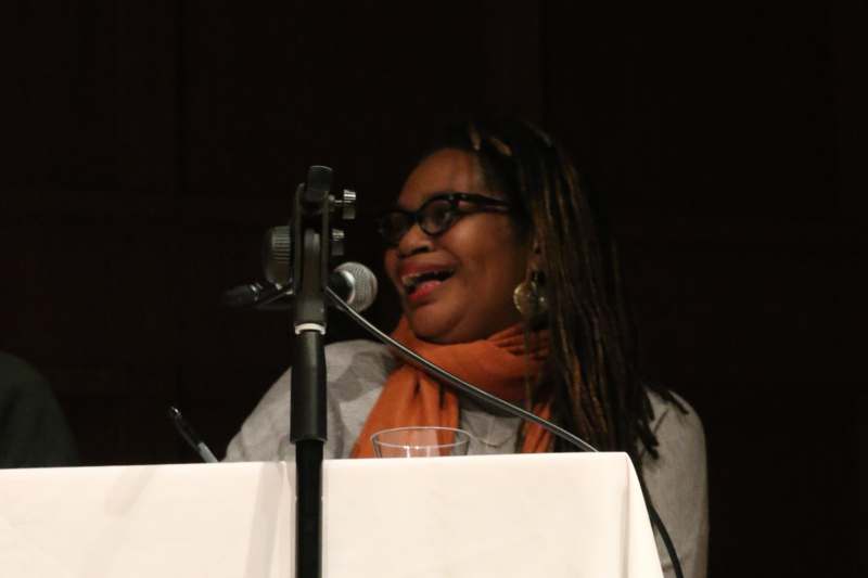 a woman with dreadlocks and orange scarf speaking into a microphone