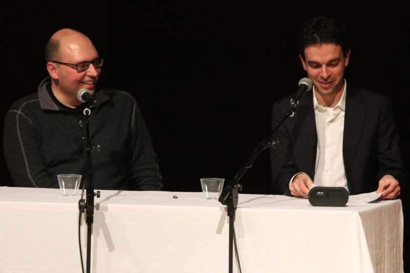 two men sitting at a table with microphones