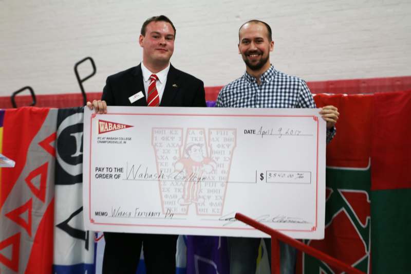 a couple of men holding a large check