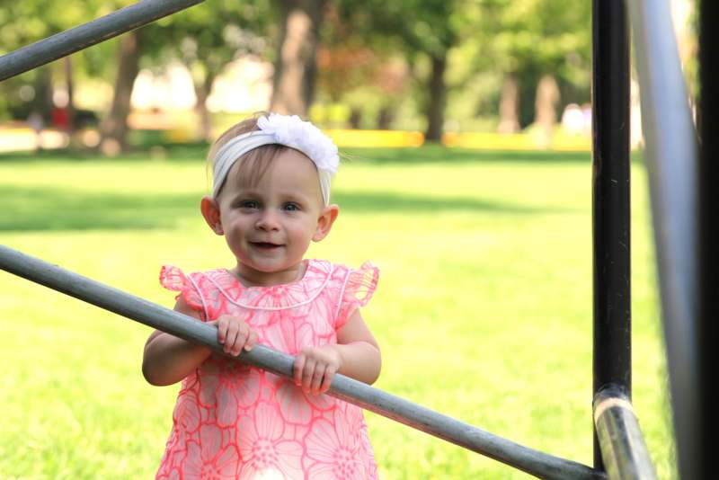 a baby girl in a pink dress holding a metal bar