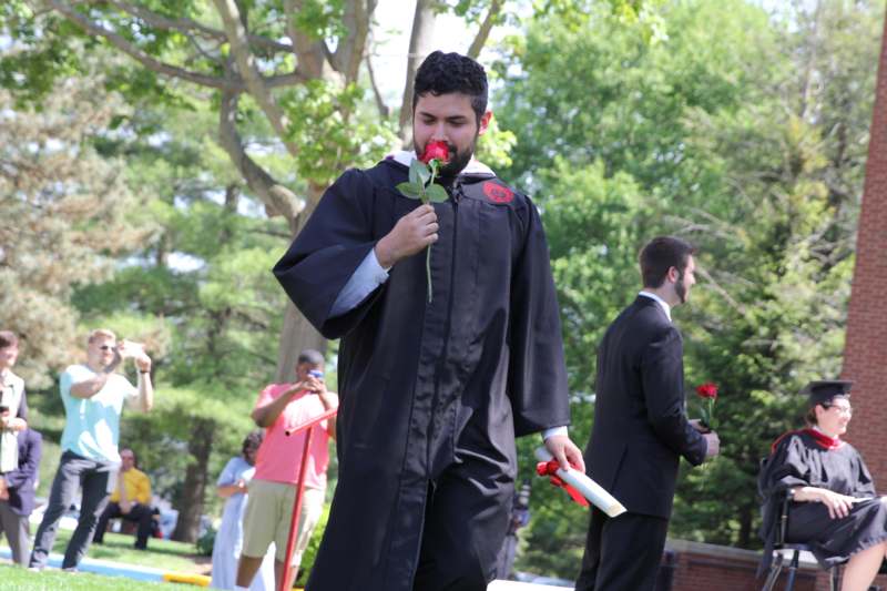 a man in a graduation gown smelling a rose