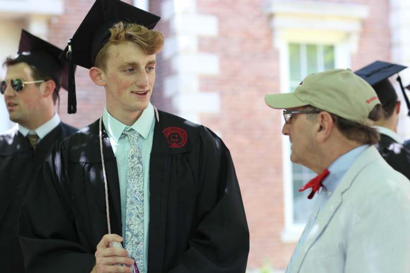 a man in a graduation gown and cap talking to a man