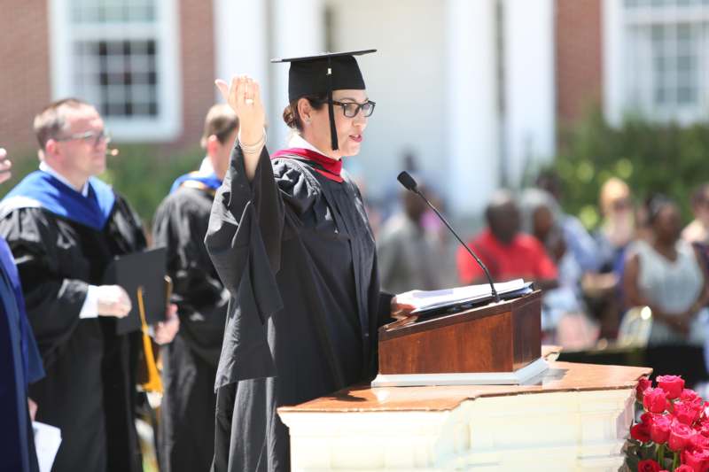 a woman in a graduation gown and cap raising her hand