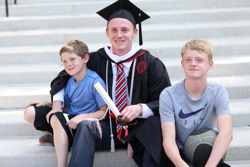 a man in a graduation gown and cap sitting on stairs