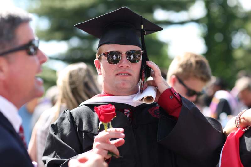 a man in a graduation gown and cap holding a rose
