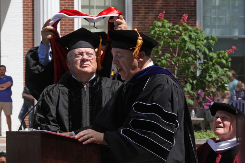a man in a cap and gown holding a scarf over another man