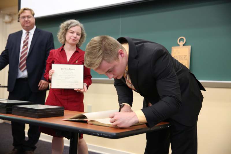 a man in a suit leaning over a table with a woman holding a certificate