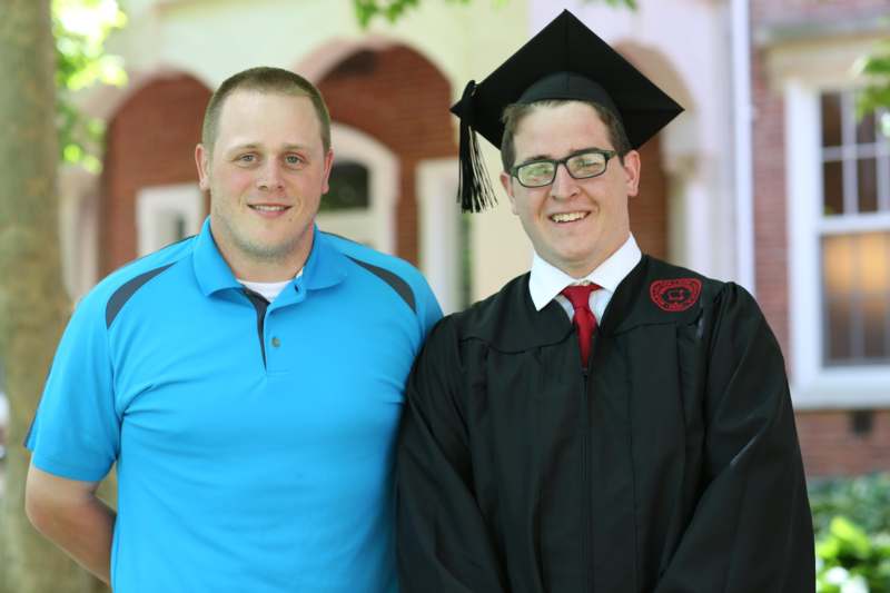 a man in a graduation gown and cap standing next to another man
