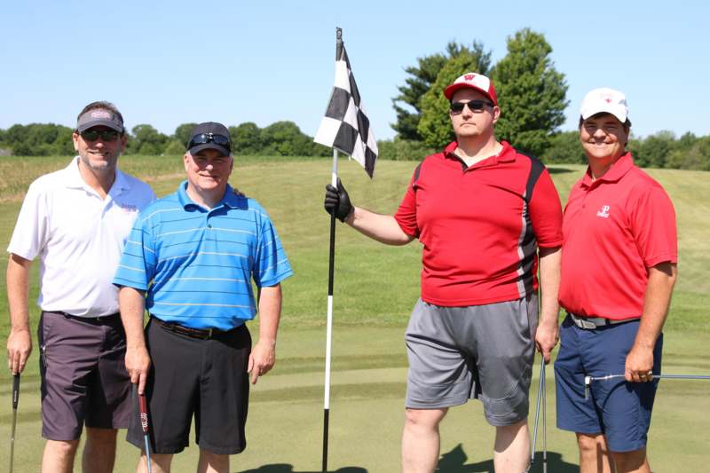 a group of men standing on a golf course holding a flag