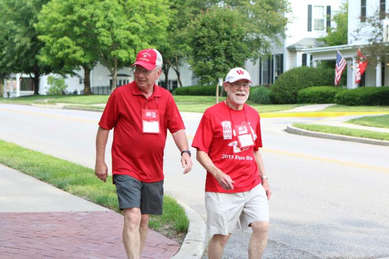 two men wearing matching red shirts and white hats walking on a sidewalk