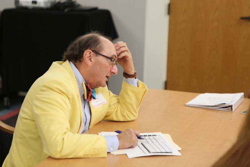a man in a yellow suit sitting at a table with papers