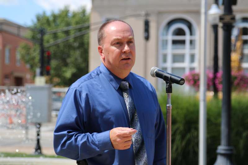a man in a blue shirt and tie speaking into a microphone