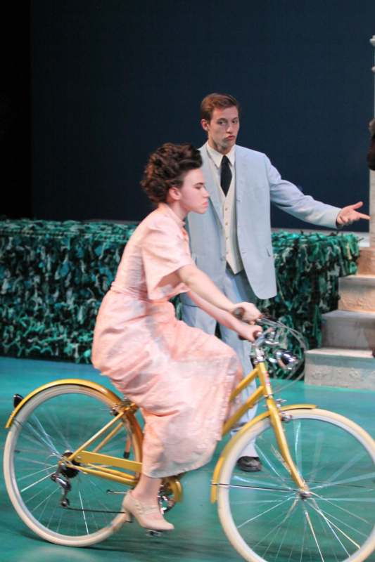 a woman in a pink dress riding a bicycle next to a man in a suit