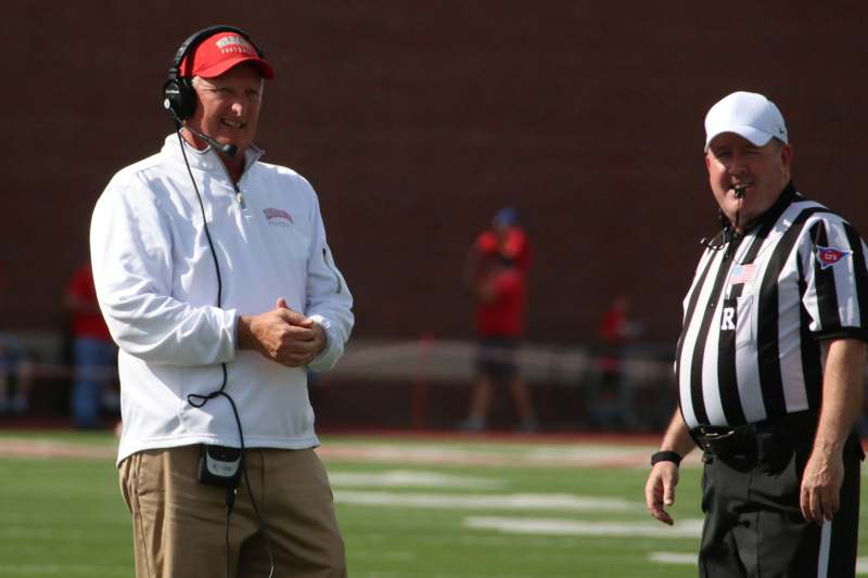 a man in a white shirt and a red hat talking to another man on a football field