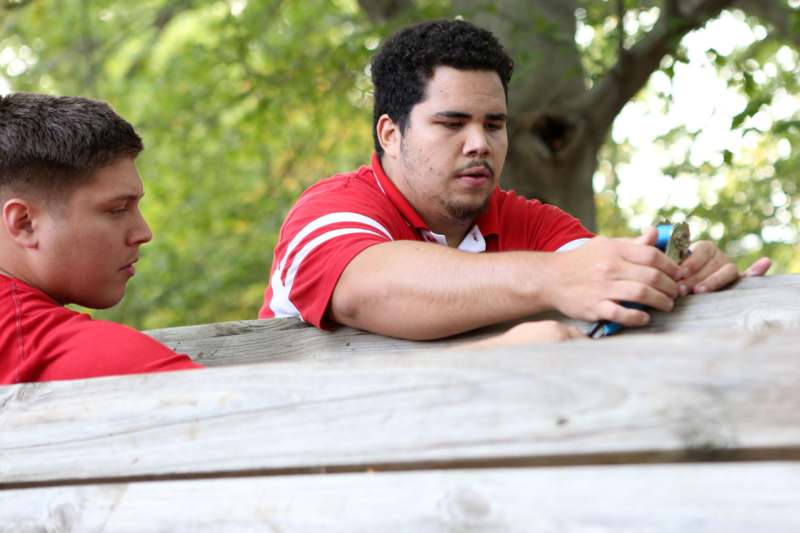 two men in red shirts leaning on a wooden fence