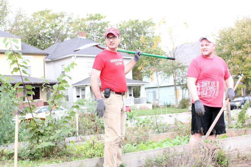 two men wearing red shirts and holding a green shovel