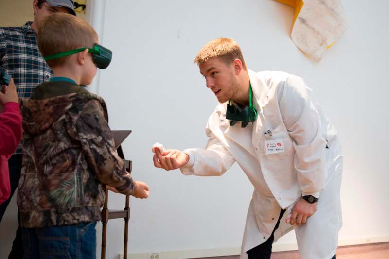 a man in a white coat and green goggles holding a boy's hand