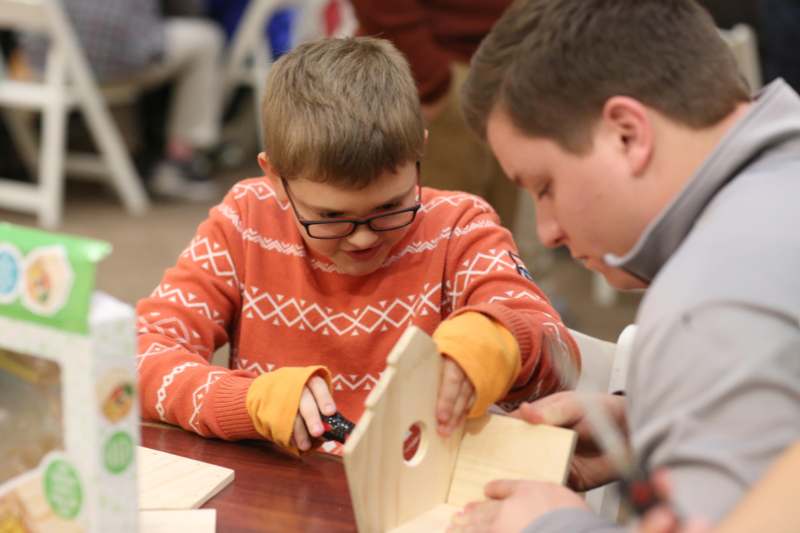 a boy with glasses and a screwdriver working on a birdhouse