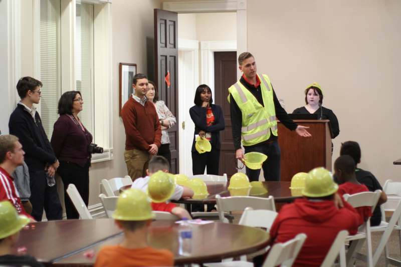 a group of people in a room with a man wearing hard hats