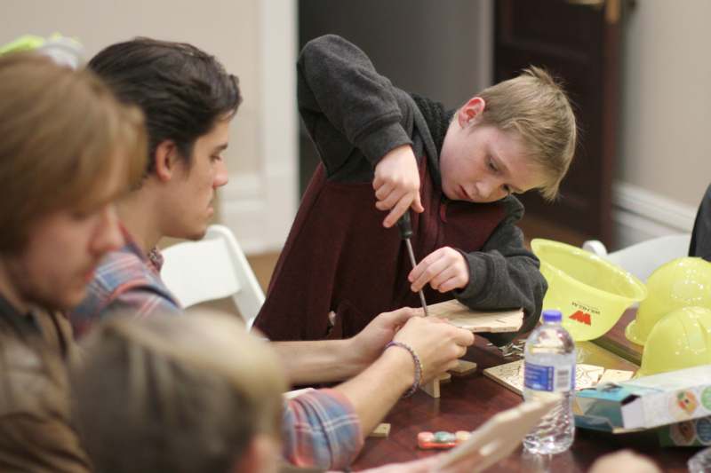 a boy holding a screwdriver while sitting at a table with other people