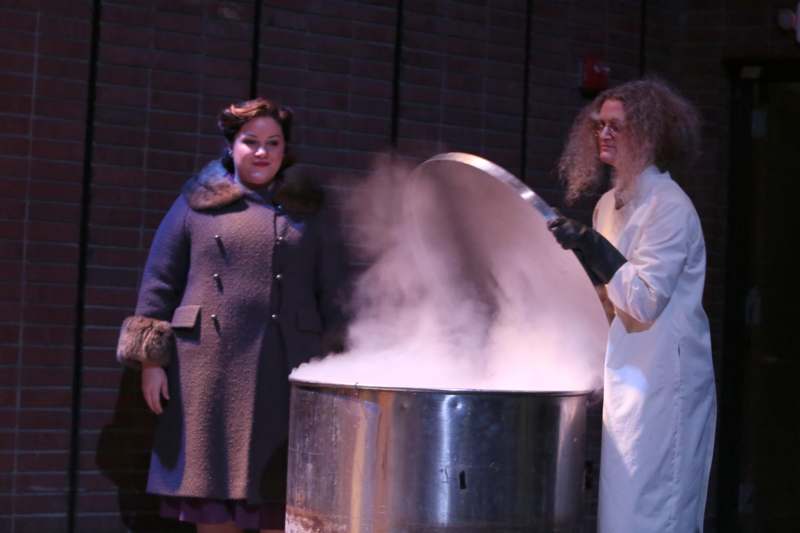 a woman in a white coat and a woman in a white coat standing next to a large metal container with liquid