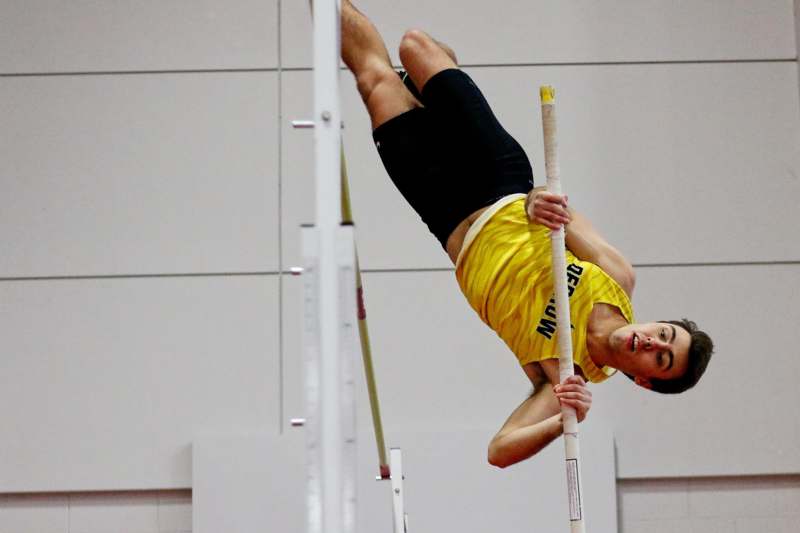 a man in a yellow shirt jumping over a pole