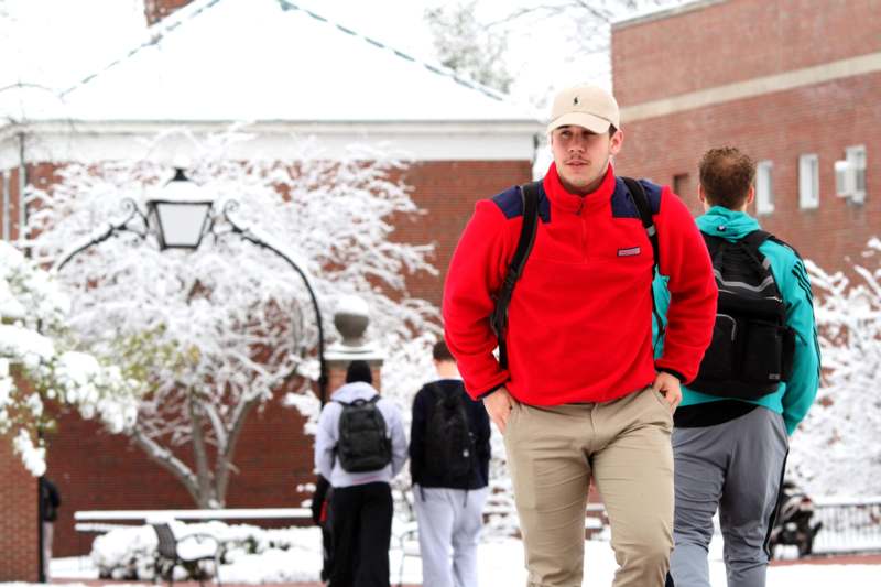 a man in a red jacket and tan cap walking in the snow