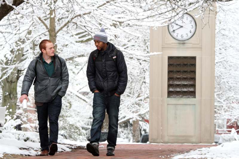 two men walking on a brick walkway with snow covered trees