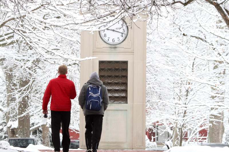 two people walking on a sidewalk with a clock