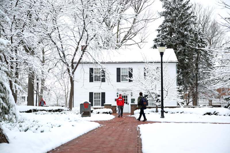 people walking on a brick path in front of a house with snow