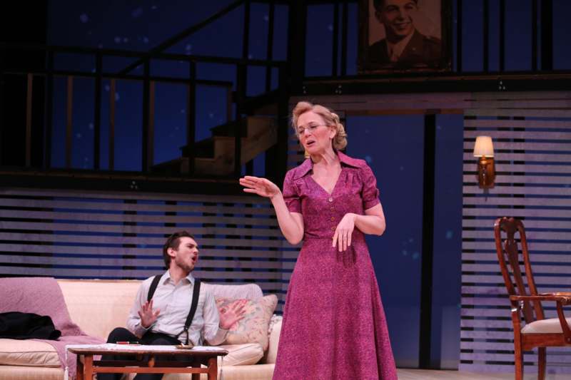 a woman in a dress on a stage with a man sitting on a couch
