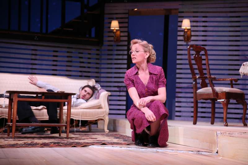 a woman in a purple dress sitting on a stage with a man lying on a couch