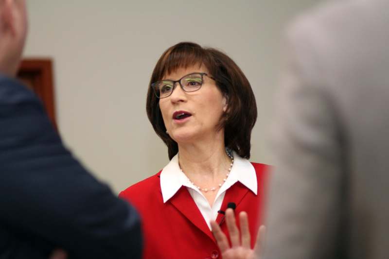 a woman in a red shirt and glasses speaking to a group of people