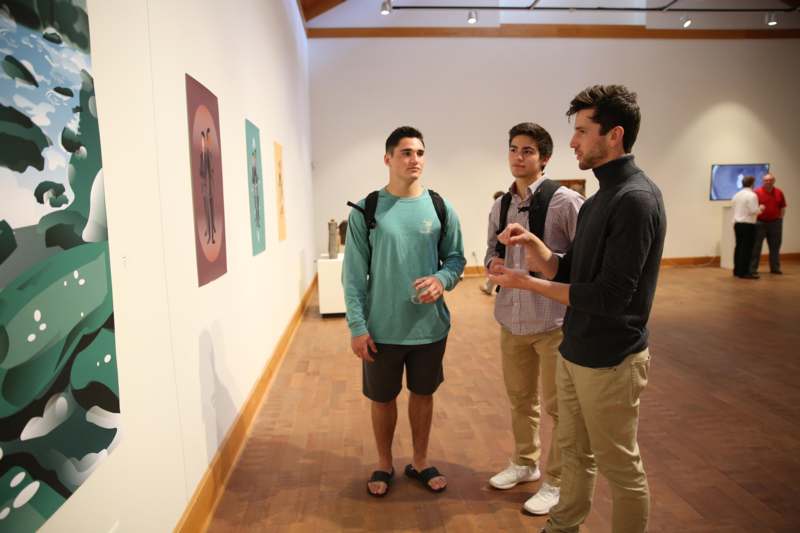 a group of men standing in a room with paintings on the wall