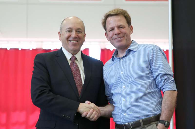 two men shaking hands in front of a red curtain