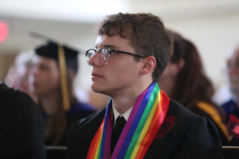 a man wearing a graduation gown and rainbow sash