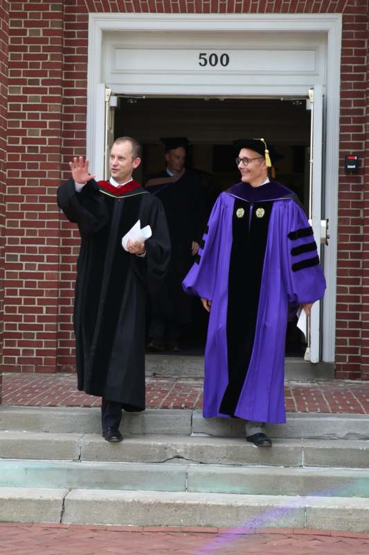 a man in a graduation gown waving to another man in a doorway