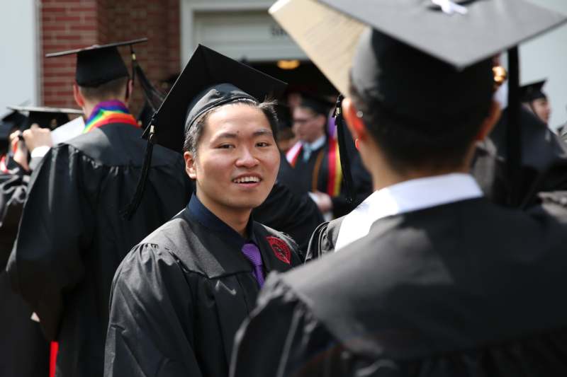 a man in black gowns and cap standing in front of other people