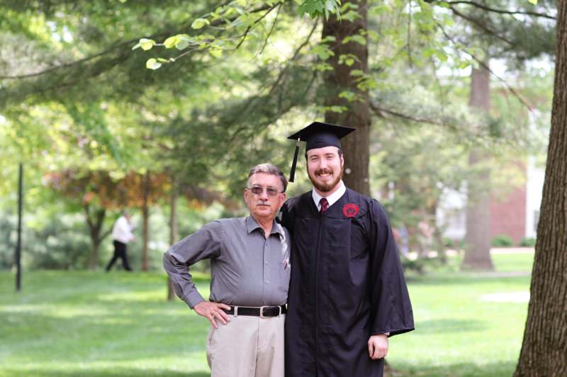 a man in a graduation gown and cap standing next to a man in a park