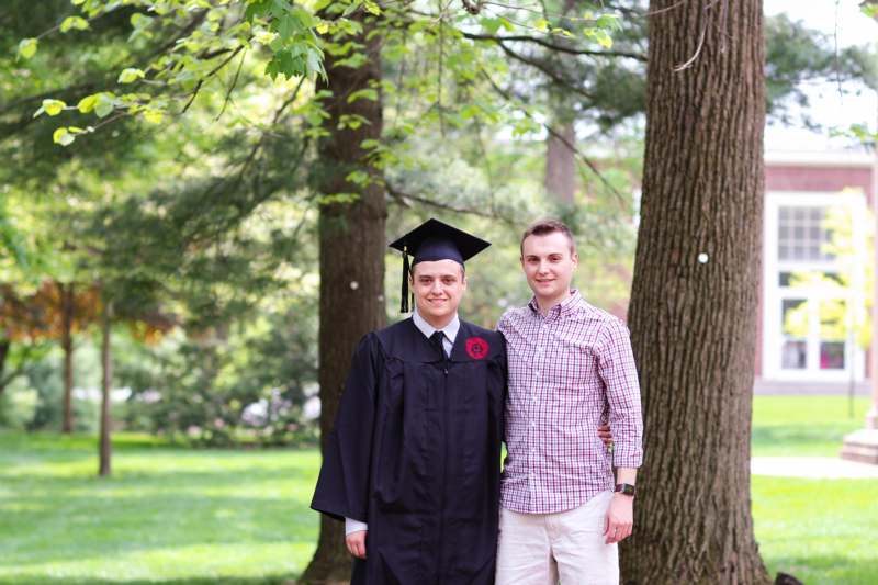 a man in a graduation gown and cap standing next to a man in a park