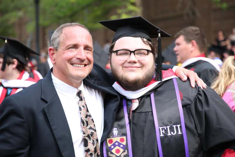 a man in a graduation gown and cap with his arm around a man