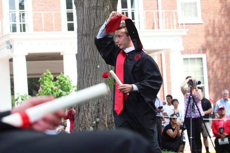 a man in a cap and gown holding a red rose and a diploma