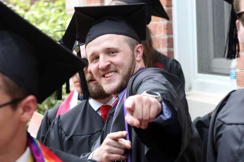 a man in a graduation gown pointing at the camera